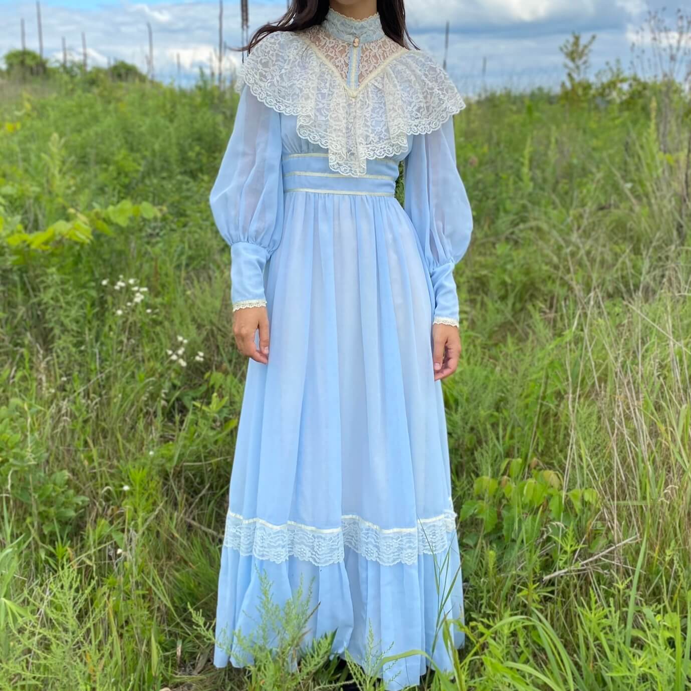 Vintage blue prairie dress with lace collar on a model in a green field