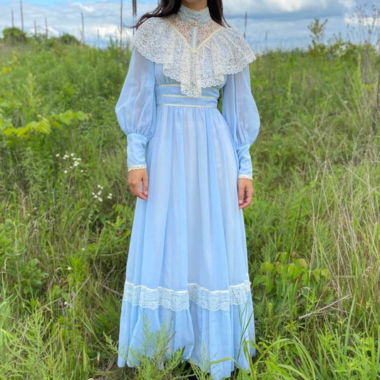 Vintage blue prairie dress with lace collar on a model in a green field