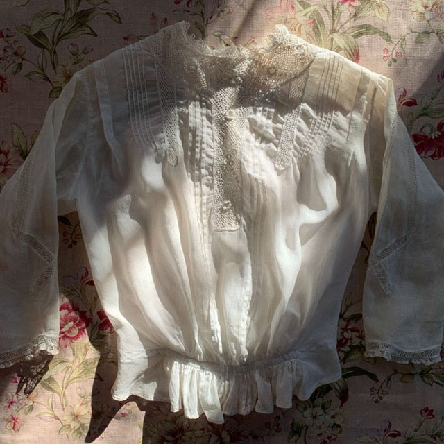 white antique blouse laid on top of pink floral fabric