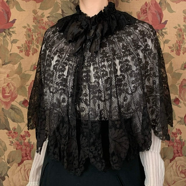 Lace capelet from the 1900s in black in front of a floral backdrop
