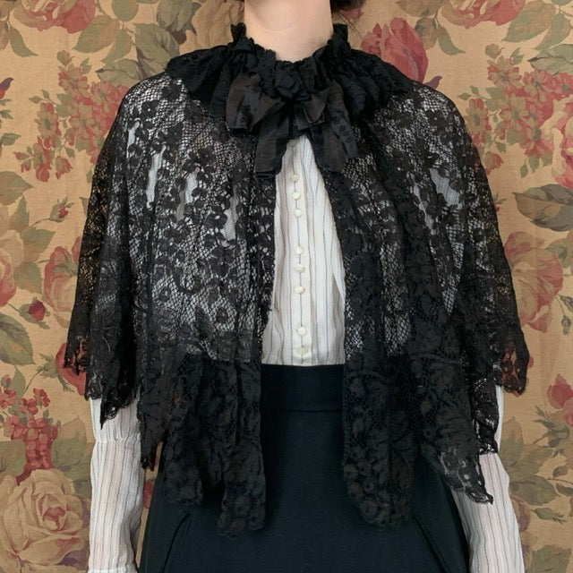 Edwardian black lace capelet with a black bow at the neck on top of a white blouse with black skirt