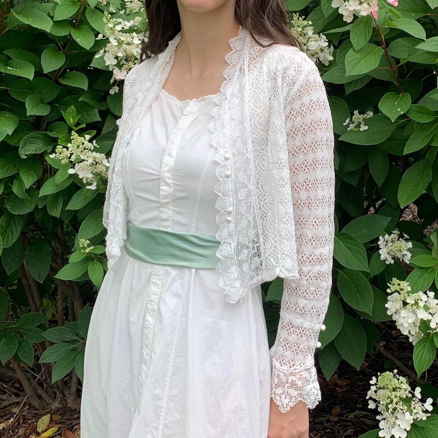 model wearing white dress and lace cardigan in front of flowers