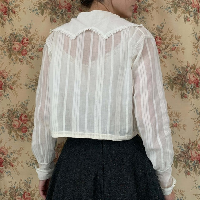 blouse shown from the back in white fabric worn with a gray skirt